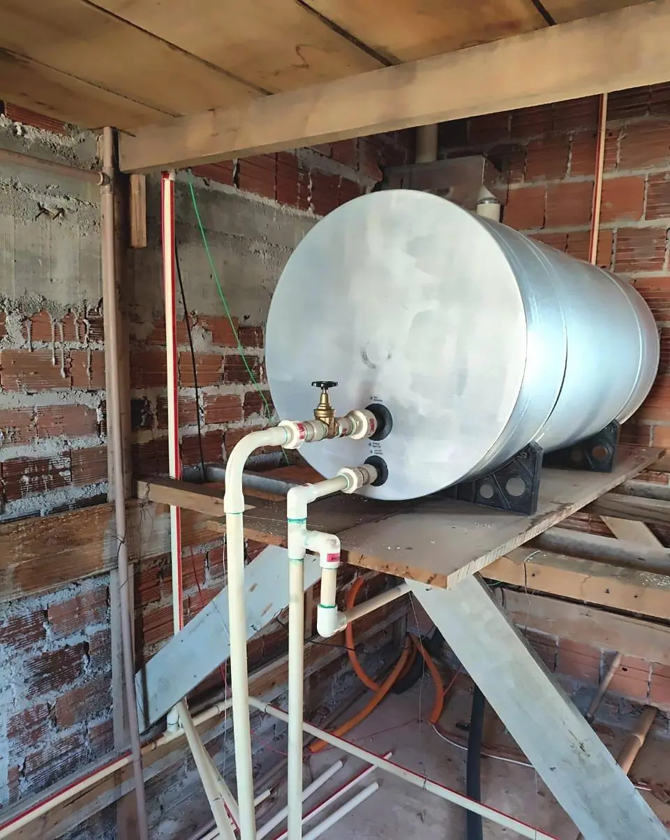 Boiler de inox deitado sobre plataforma de madeira, com tubulação de CPVC e registro de bronze, em obra