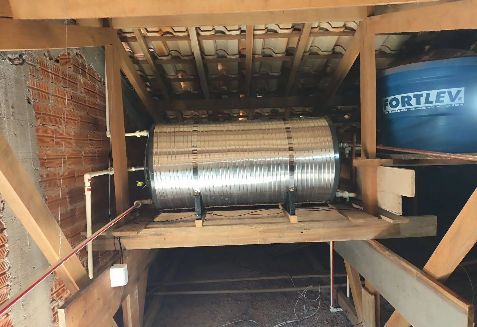Boiler cilíndrico de inox instalado sob o telhado, em plataforma de madeira, com tubulação de CPVC ligada ao reservatório