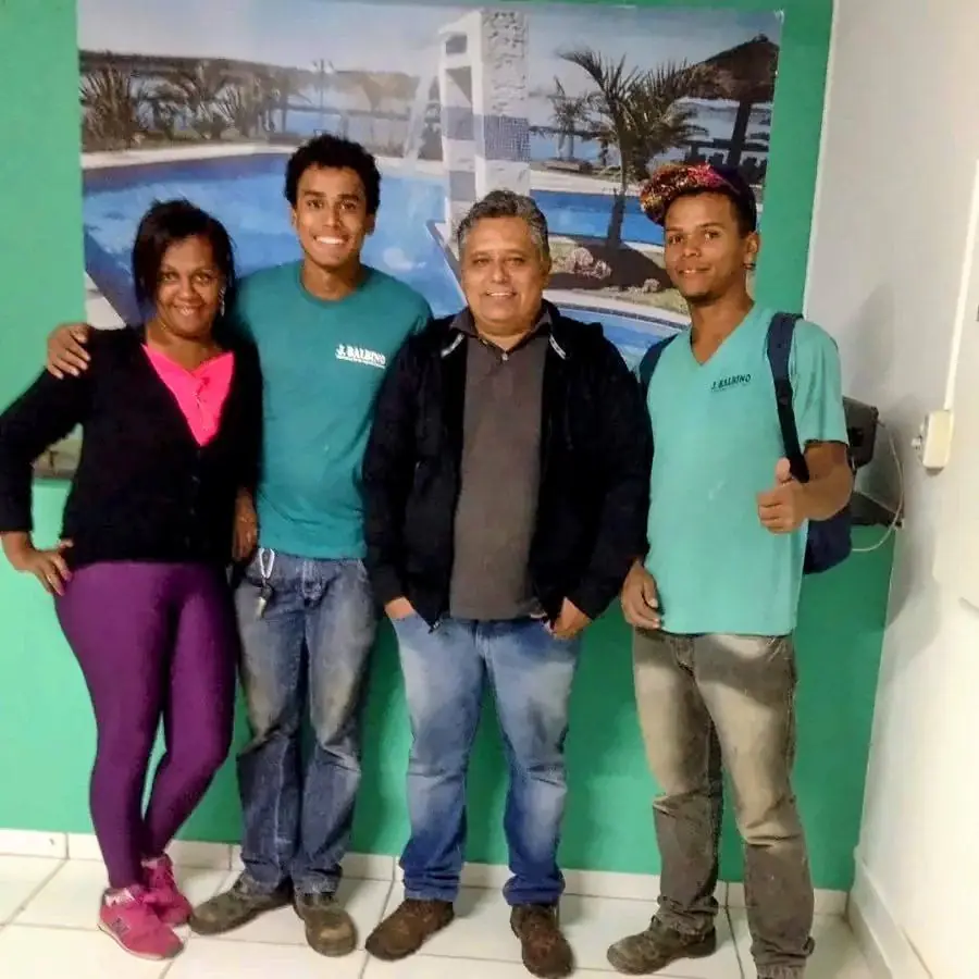 Equipe da J. Balbino reunida dentro da loja, diante de um painel com foto de piscina