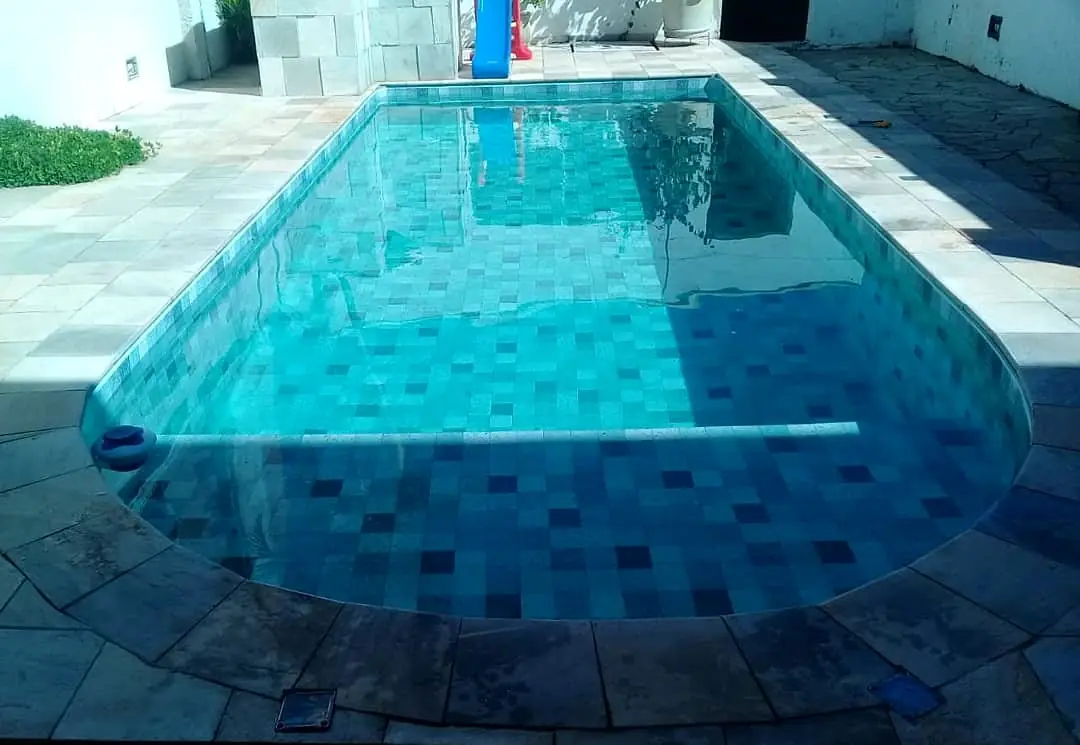 Piscina de vinil com borda arredondada já cheia, em área externa com piso de pedra
