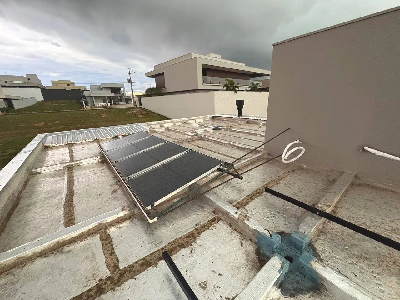 Coletores solares instalados em laje de casa em condomínio, vistos de cima, com céu carregado ao fundo